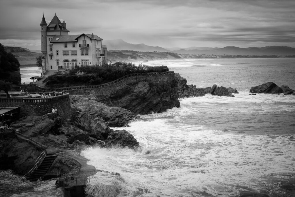 La costa de Biarritz donde destaca Villa Belza con el mar agitado y las o las rompiendo contra las rocas, fotografía en blanco y negro