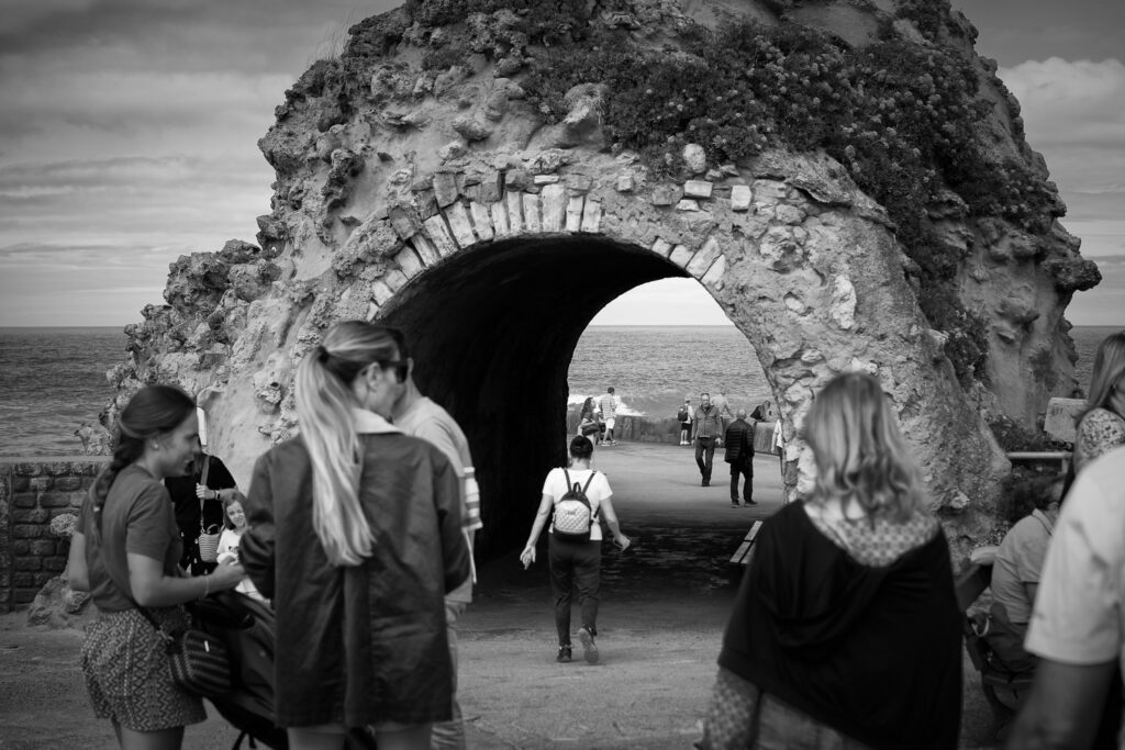 Formación rocosa con un túnel por el que pasa la gente para ir a ver el mar, fotografía en blanco y negro