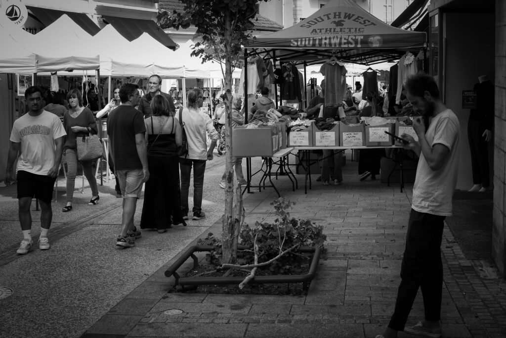 Un chico mira su smartphone mientras otro chico le mire fijamente mientras pasea por el mercado, fotografía en blanco y negro