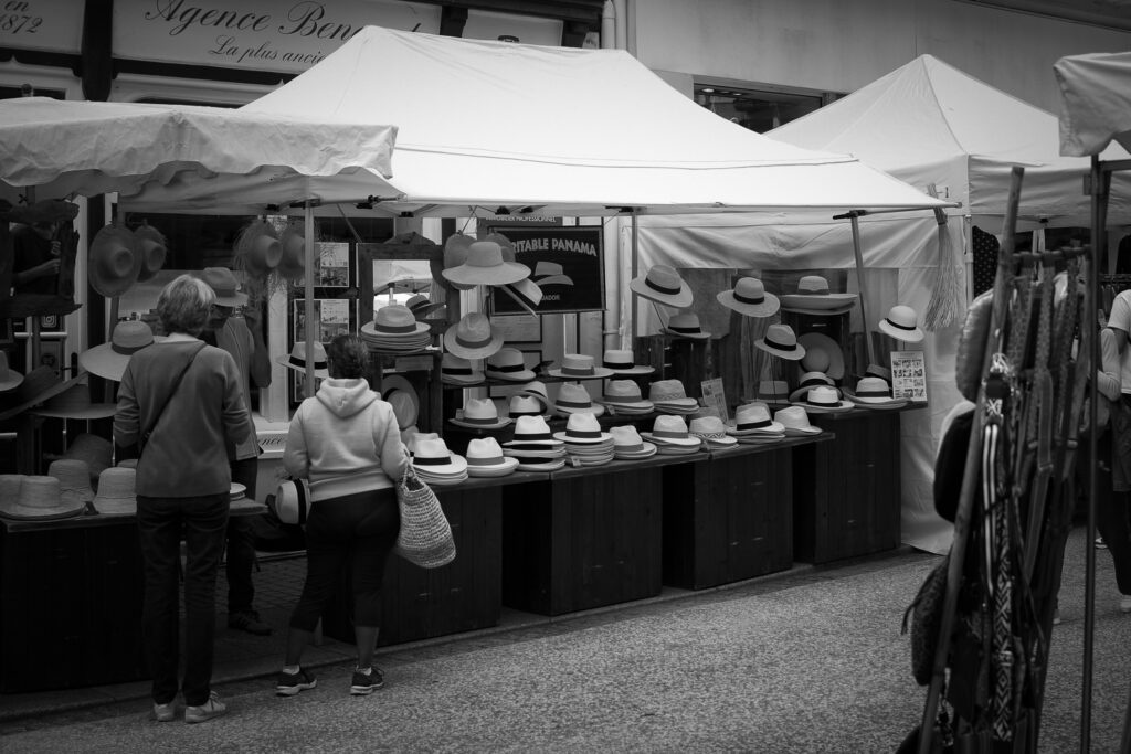 Unas personas observan un puesto de sombreros de paja en el mercado de Biarritz, foto en blanco y negro