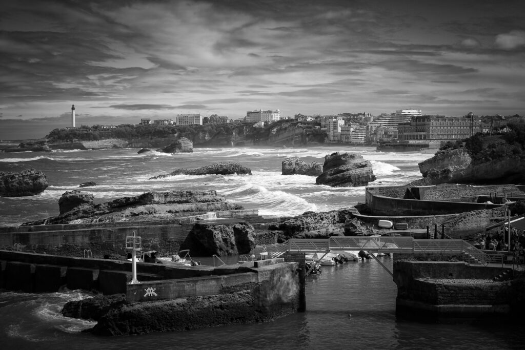 Imagen le Port des Pêcheurs en Biarritz con olas, rocas y parte de la costa con el faro al fondo, fotografía en blanco y negro