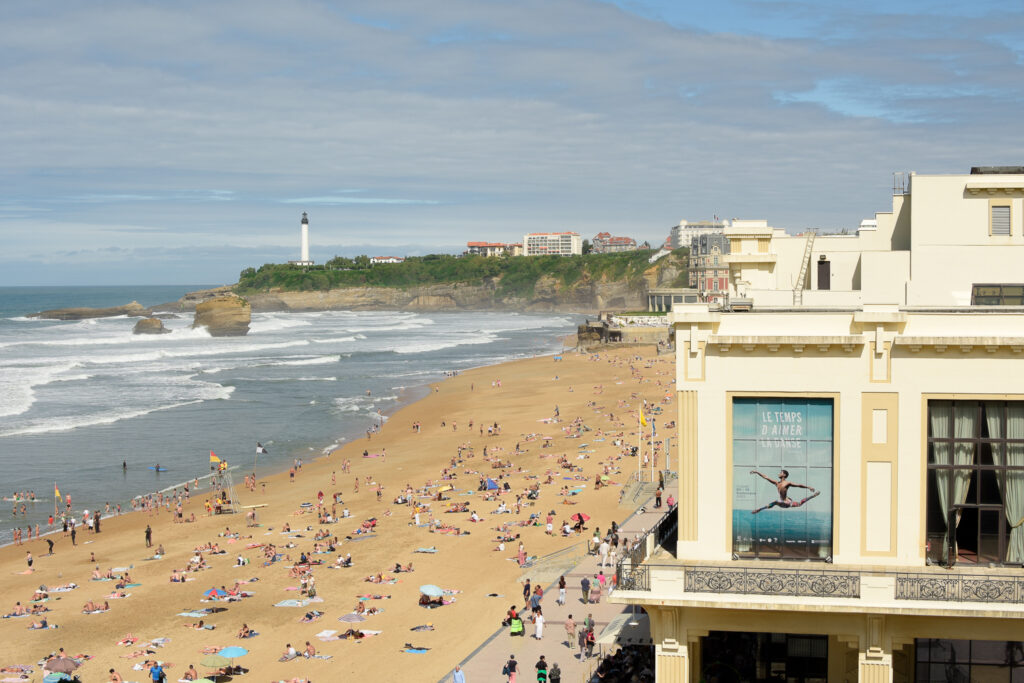 Gente disfrutando de la playa de Biarritz, parte del casino y faro al fondo
