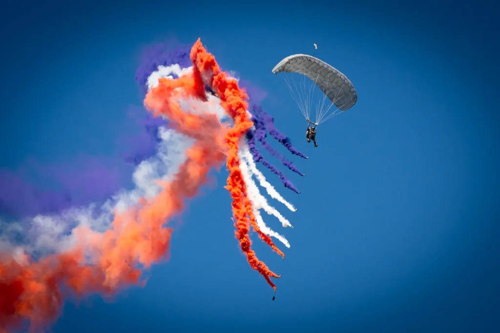 Paracaidista con estelas de humo de colores violeta, blanco y naranja
